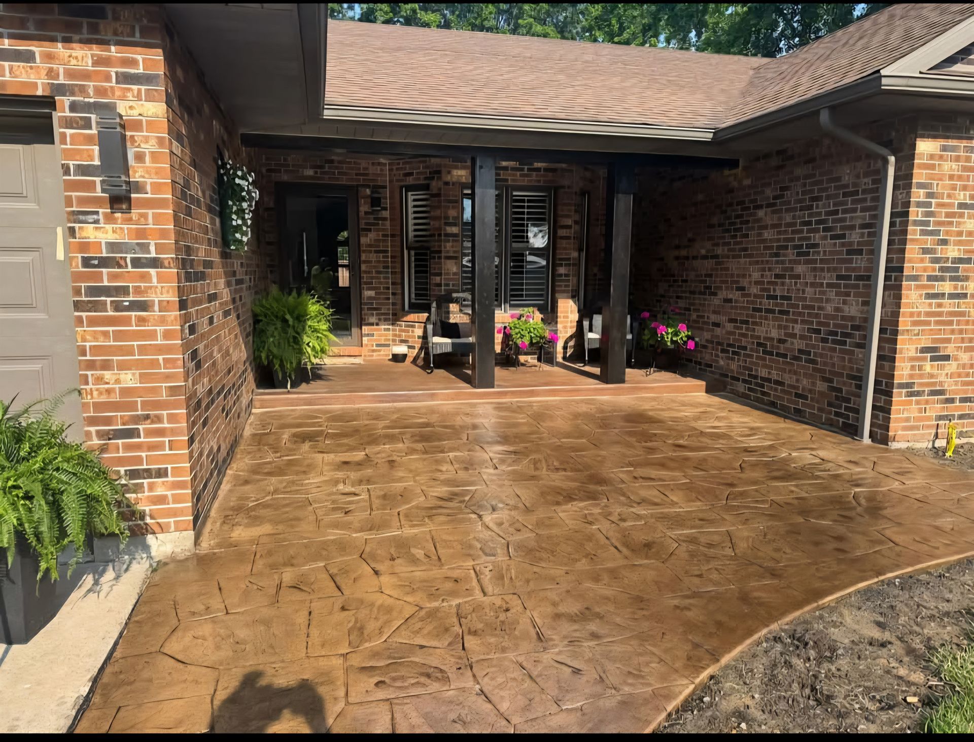 Brown stamped concrete patio in front of a brick house with dark support beams.