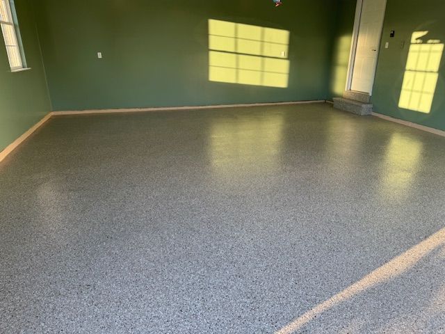 Garage interior with a gray epoxy floor, green walls, and sunlight streaming through windows.