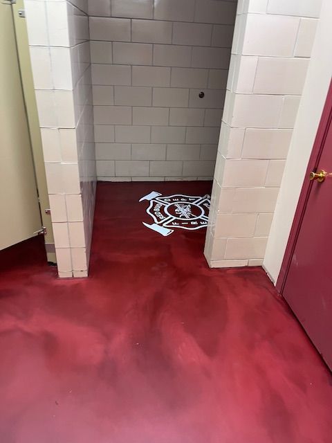 Red floor and white tile shower stall. A team logo is on the floor. A red door is on the right.