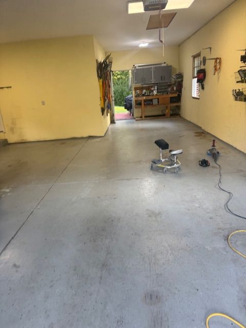 Garage interior with yellow walls, concrete floor, tools, and a glimpse of outside.