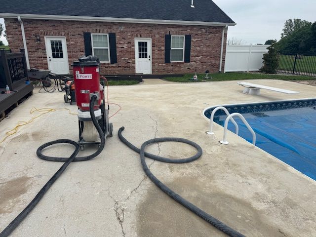 A red concrete resurfacing machine on a concrete patio near a pool and brick building.