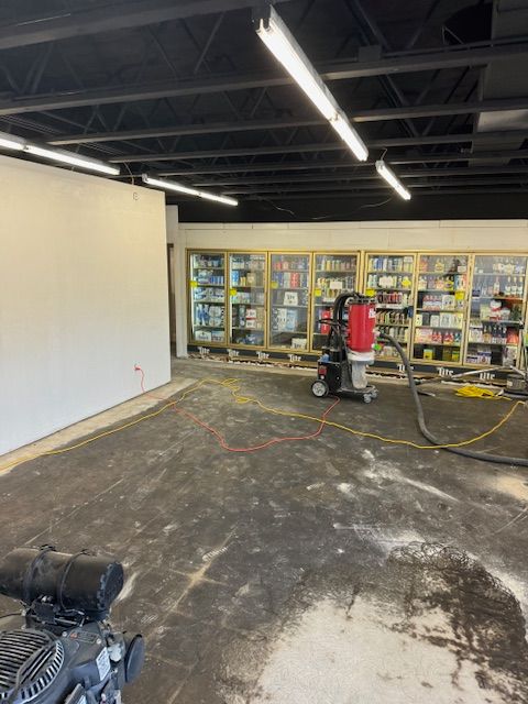 Interior view of a store under construction. Walls, shelving, equipment, and black ceiling are visible.