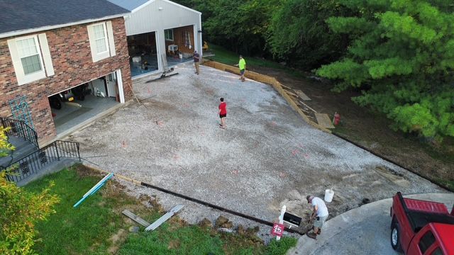Construction site: Workers preparing a concrete driveway with a house and garage in the background.