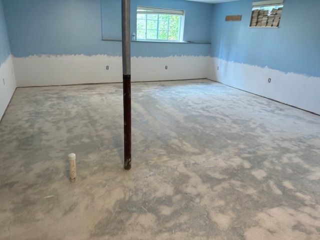 Empty basement with concrete floor, blue and white painted walls, and a support pole.