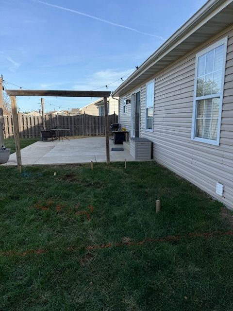 Backyard with patio, grass, and pergola. House is visible. Stakes in the grass indicate a planned project.
