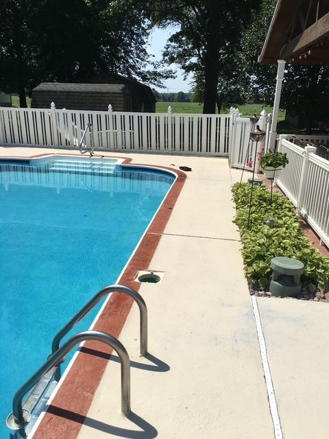 A swimming pool with white fencing. The pool has a red border and stainless steel ladder. Green plants grow alongside a path.
