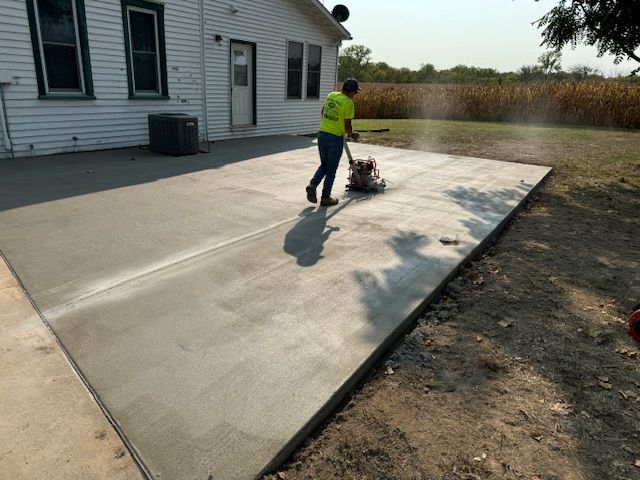 A worker uses a concrete grinder on a new patio. House in the background.