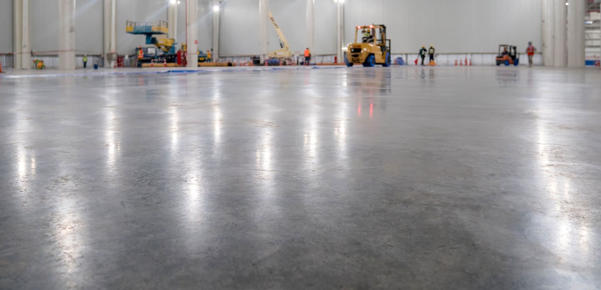 Large, polished concrete floor in a warehouse with construction vehicles and workers in the background.