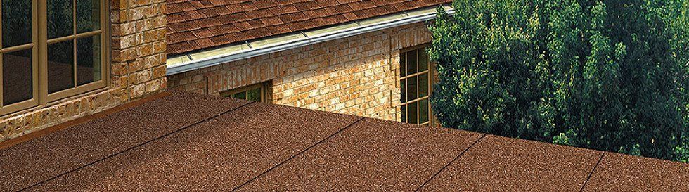 View of a building with a brown textured roof, stone walls, and green trees in the background.