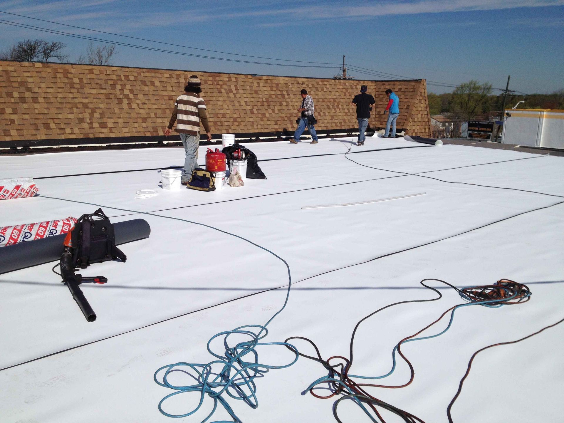 People working on a flat roof covered in white material. Tools, ropes, and supplies are scattered across the surface.