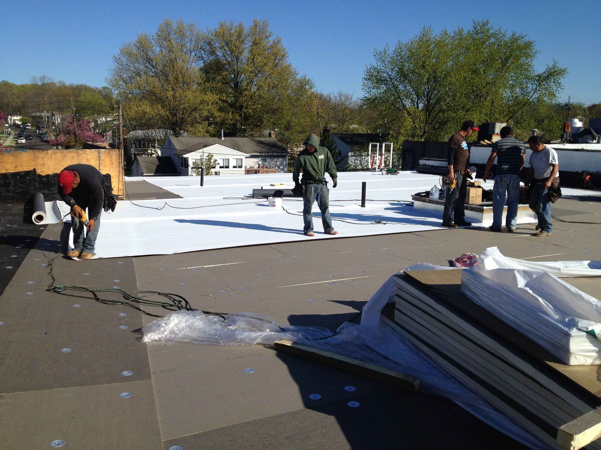 Roofers installing a white membrane on a flat roof. Several workers are present on a sunny day.