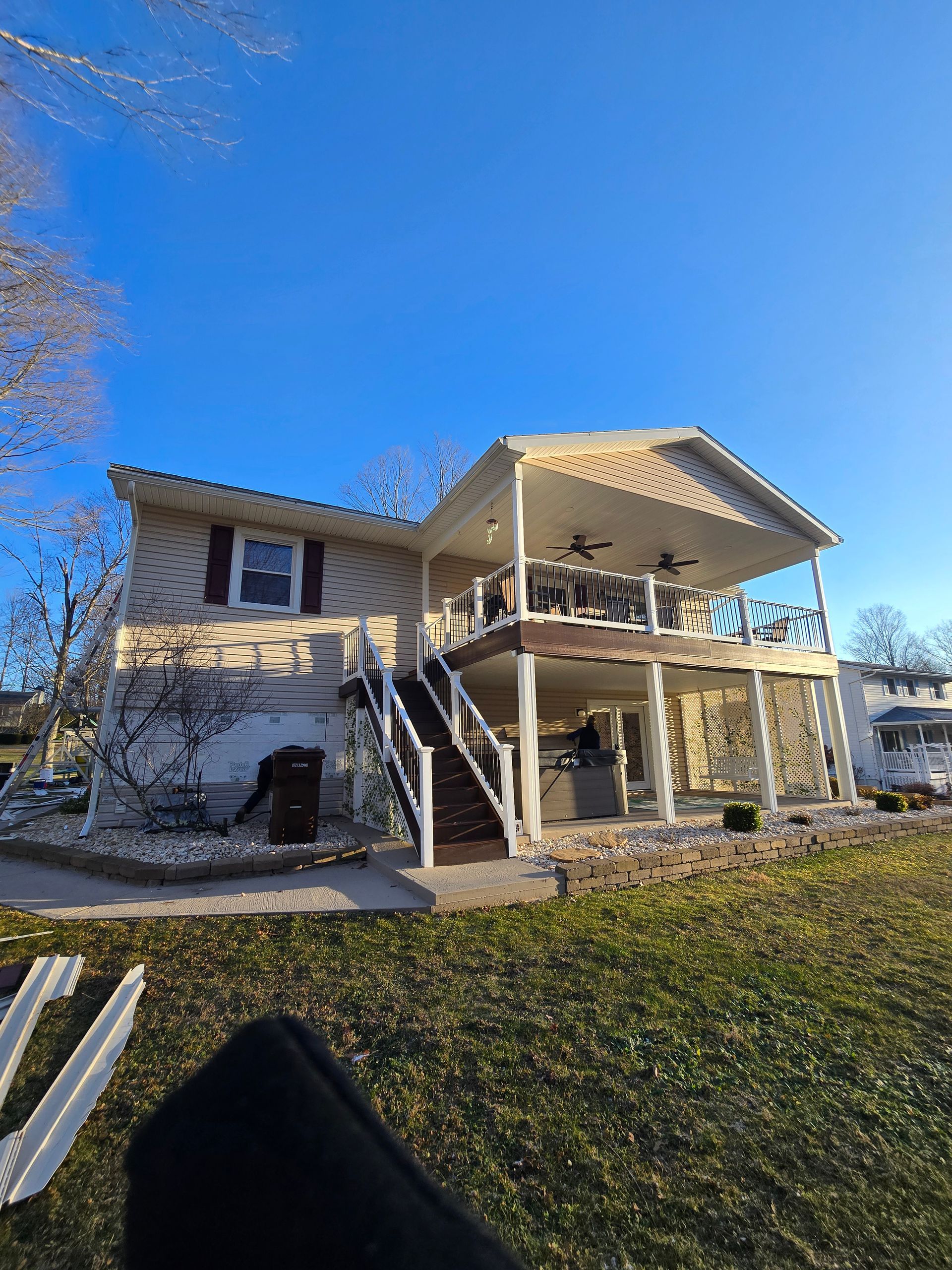 A house with a large porch and stairs is sitting on top of a lush green field.