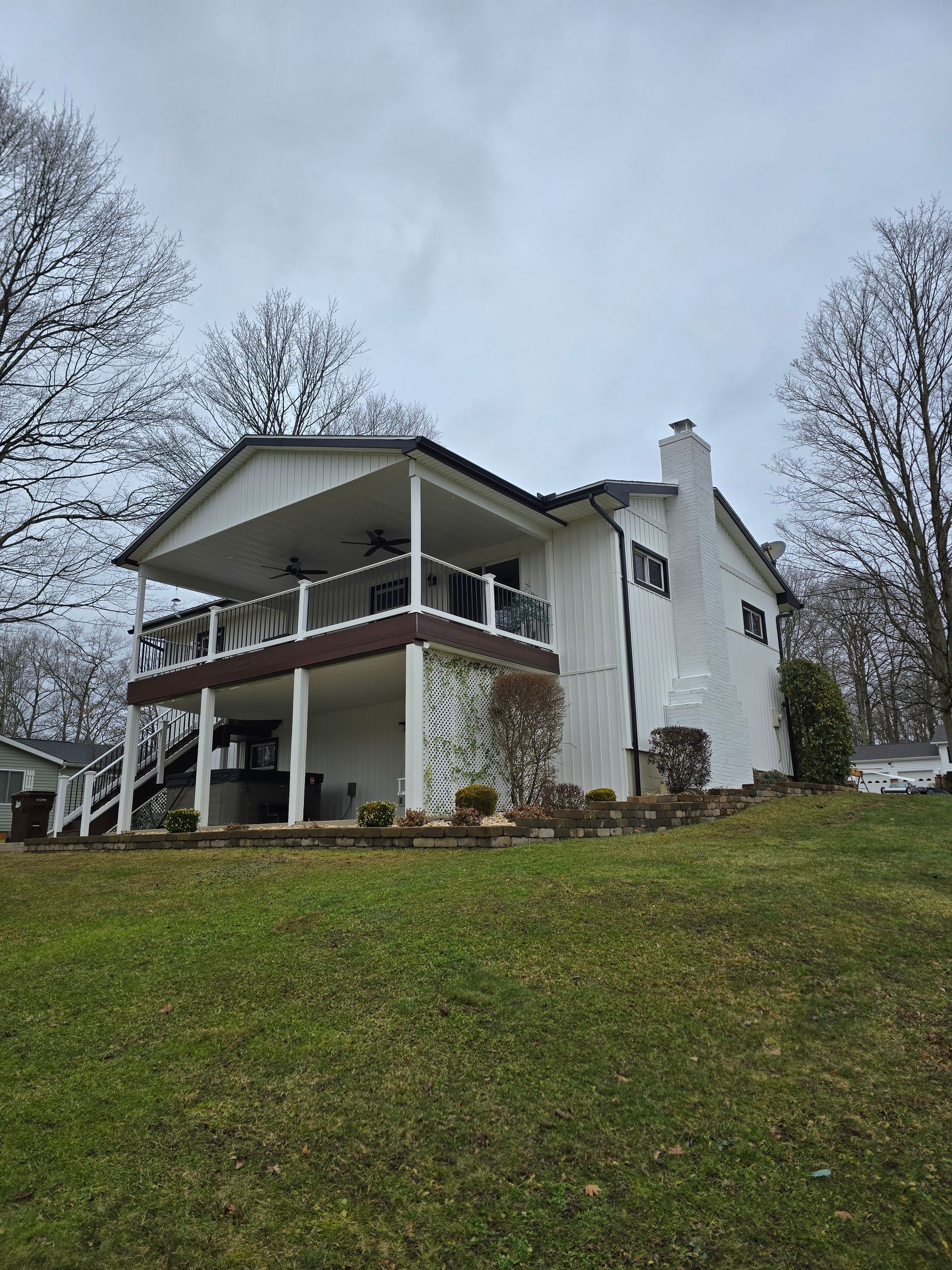 A large white house with a large deck is sitting on top of a grassy hill.