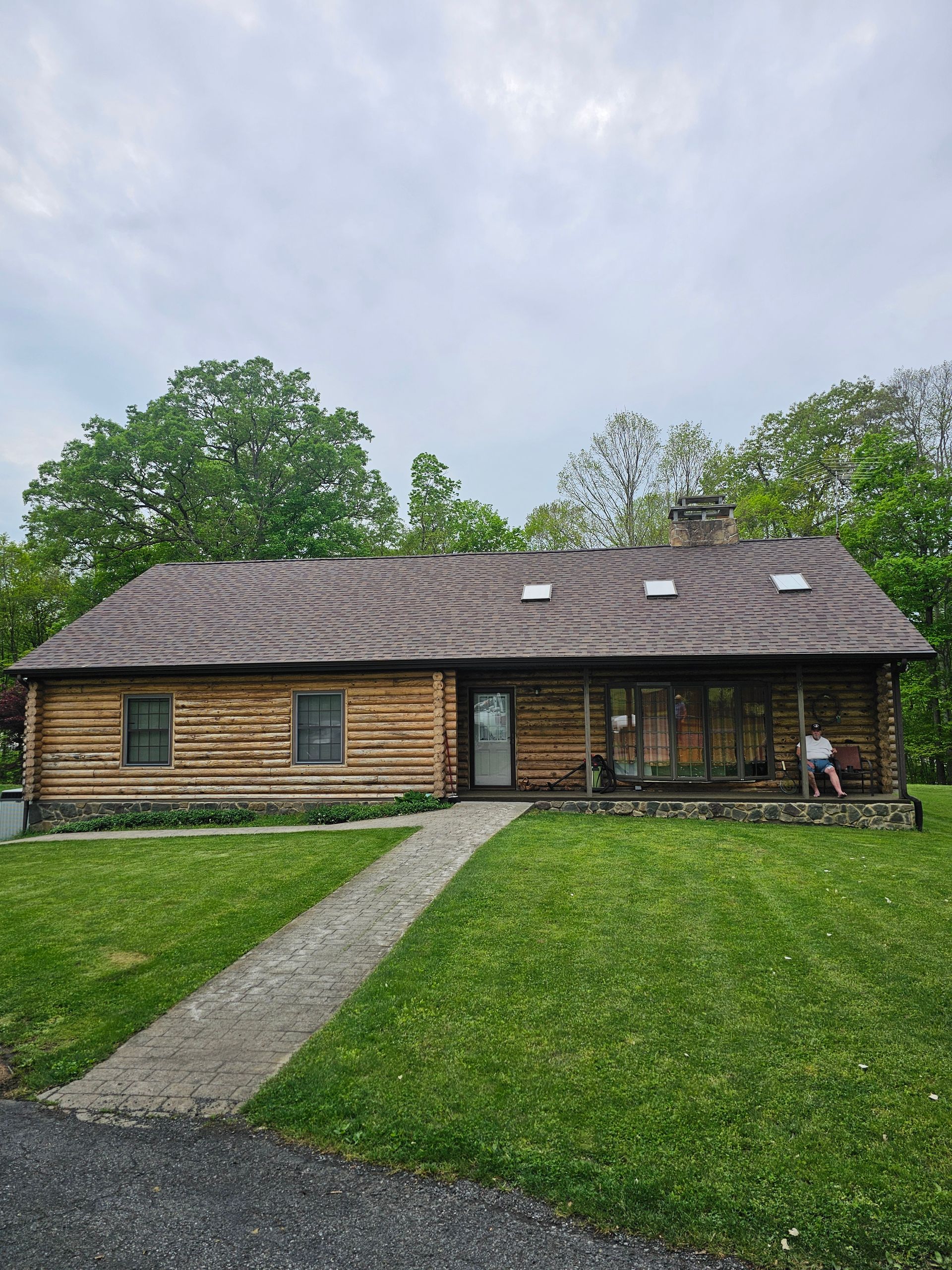 A log cabin with a shingle roof is sitting in the middle of a lush green field.