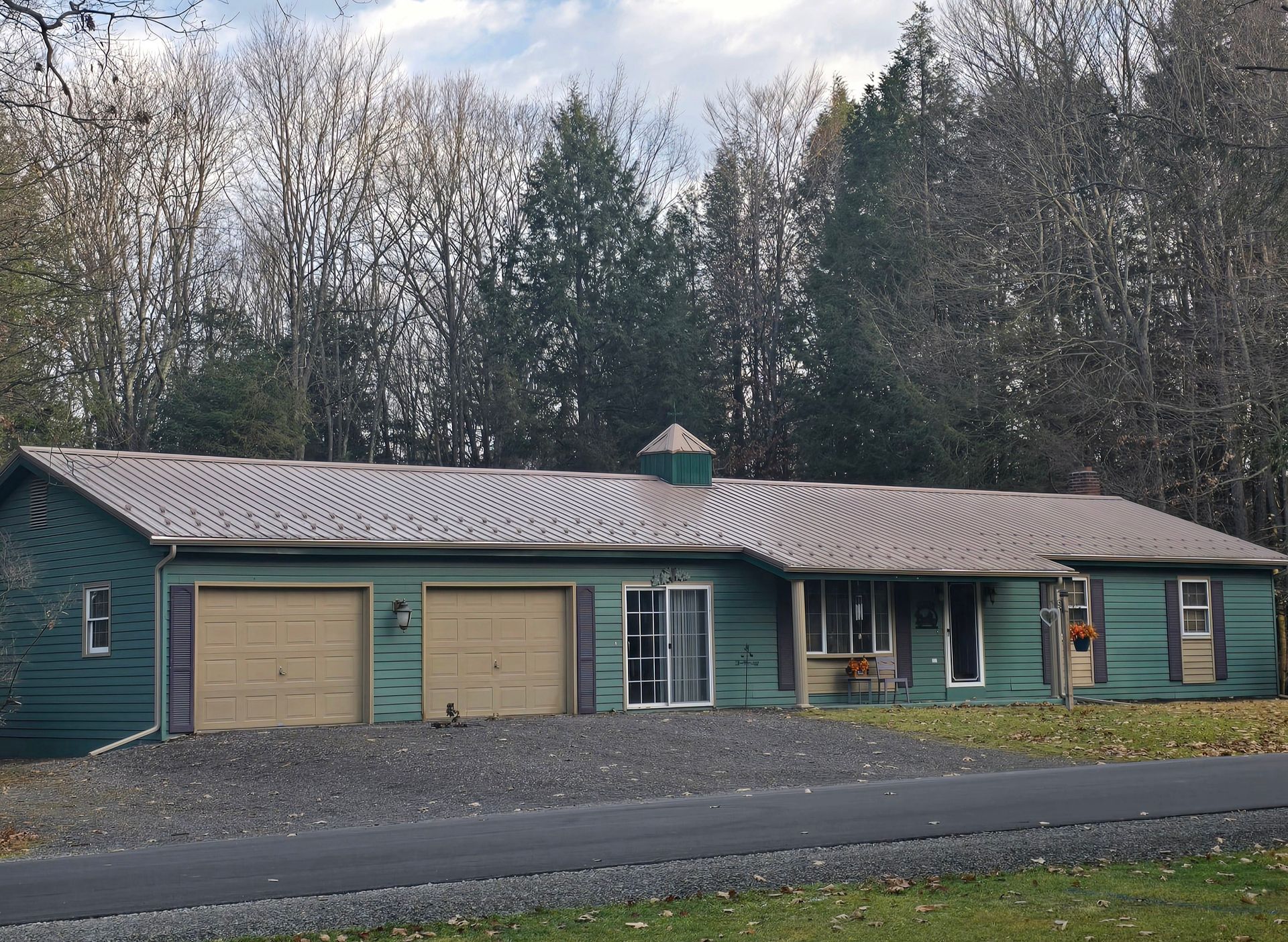A green house with two garage doors is surrounded by trees