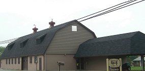 Gray barn-style building with a dark roof and small sign by the entrance