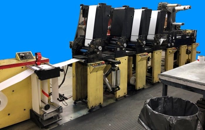 Industrial printing press with multiple yellow modules and white paper feeding through, in a factory setting.