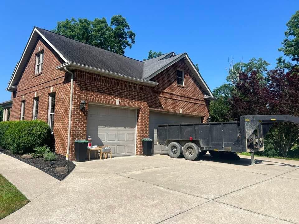 A brick house with a two-car garage. A trailer sits on the driveway beside the garage.