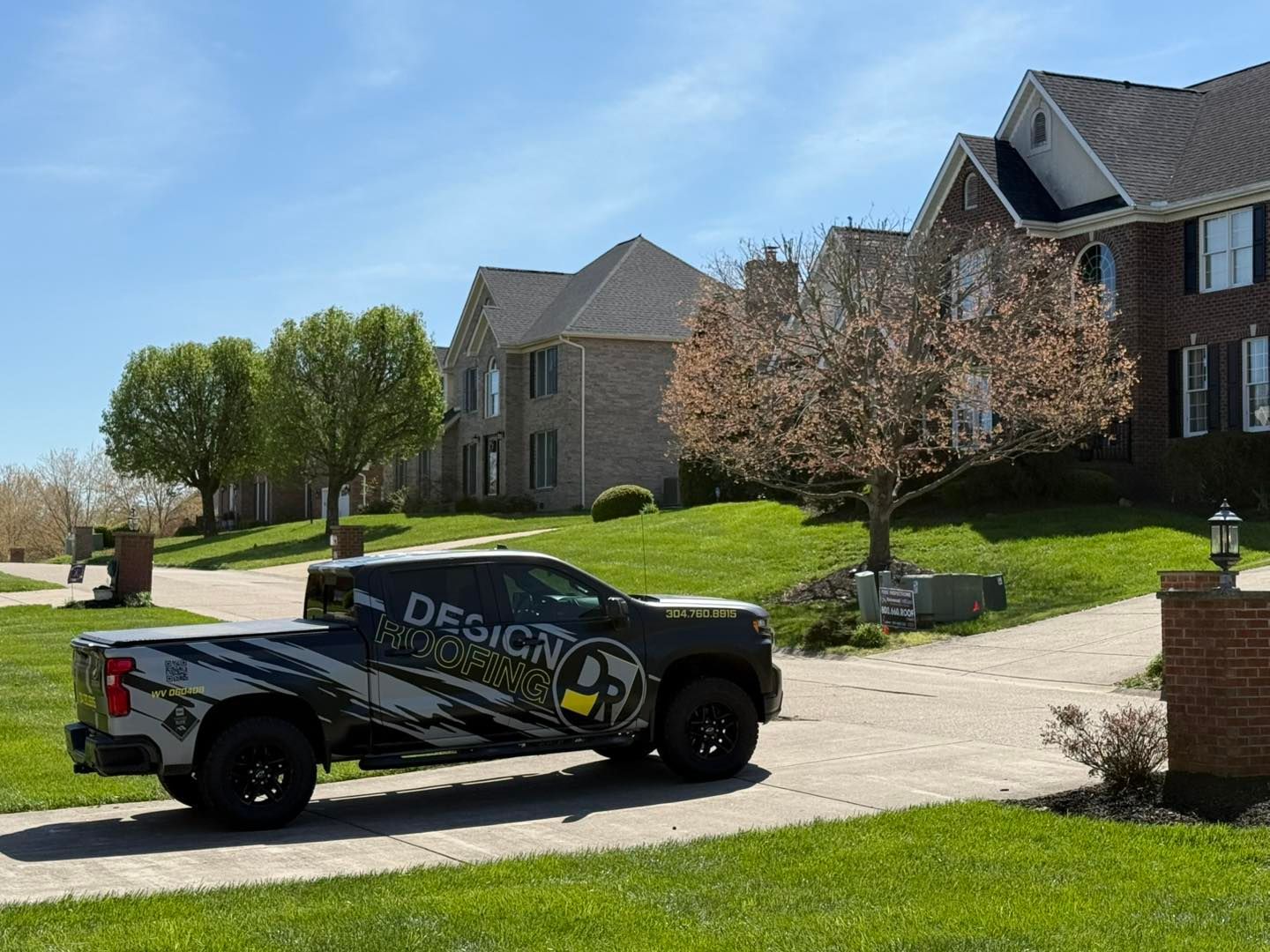 A truck with a company logo parked in front of large houses on a sunny day. The truck is on a driveway with a grassy lawn.