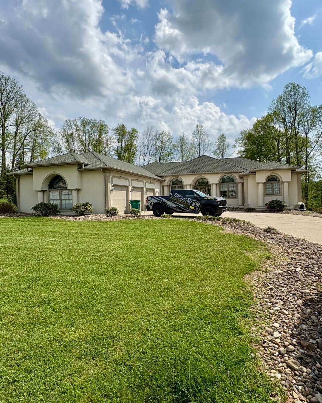 A large beige house with a black truck parked in front on a grassy lawn. Cloudy sky overhead.