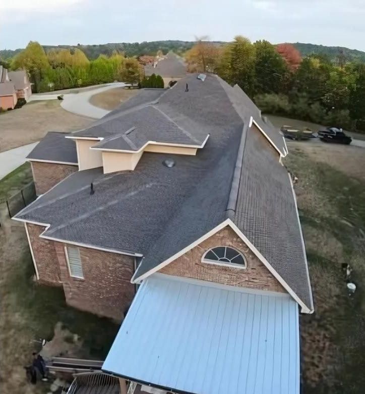Man in hard hat and safety harness, pointing, in front of trees and a building; Design Roofing logo visible.