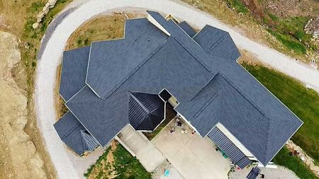 Aerial view of a modern house with a dark roof and winding driveway on a hillside.