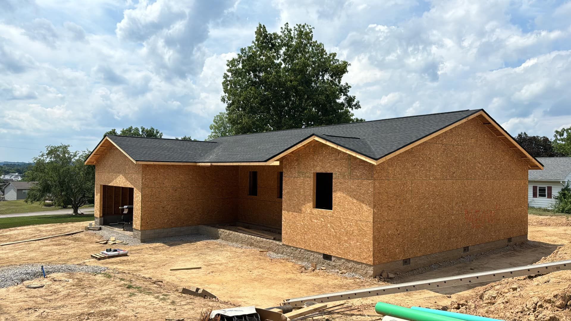 Man in a pink shirt, hard hat, and harness stands outside near trees and a building. Design Roofing logo is in the upper right corner.