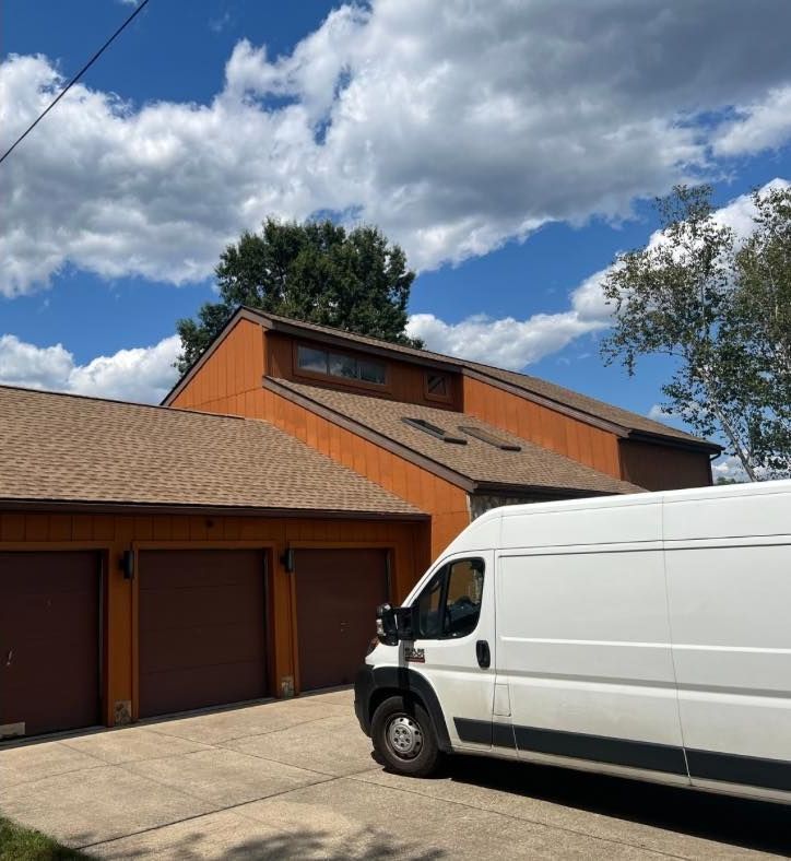 Roofers wearing safety harnesses working on a brick house roof in Hurricane, WV. The company logo reads Design Roofing.