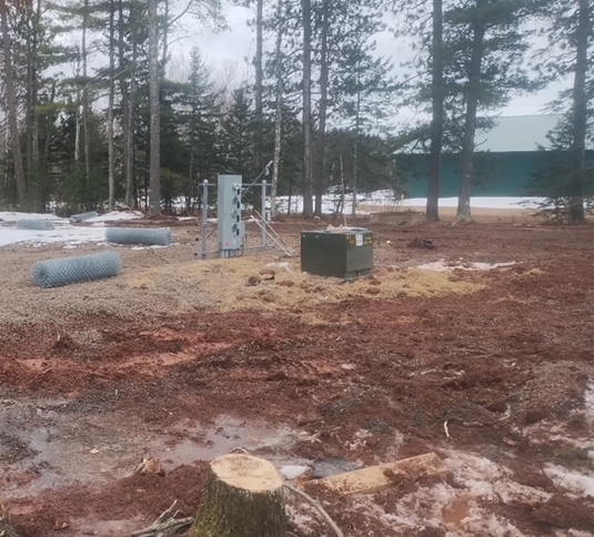 A stump in the middle of a dirt field with trees in the background.