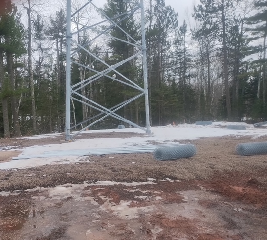 A large metal tower is in the middle of a snowy field surrounded by trees.