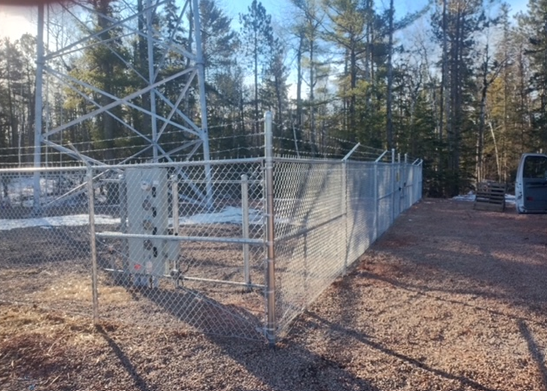 A chain link fence is surrounding a building in the middle of a dirt field.