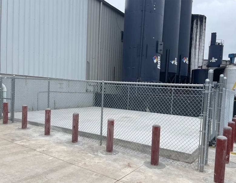 A chain link fence surrounds a concrete area in front of a building.
