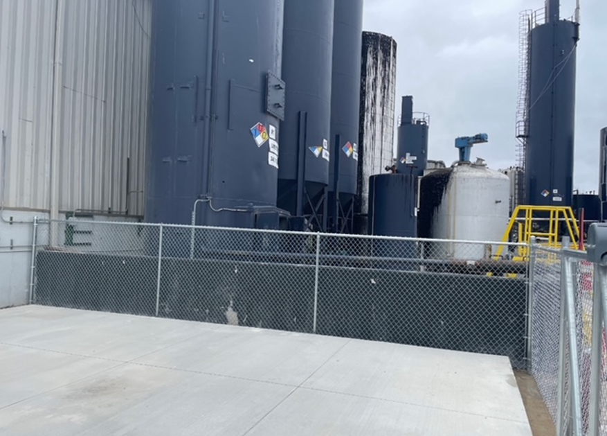 A chain link fence surrounds a large industrial area with a lot of tanks.