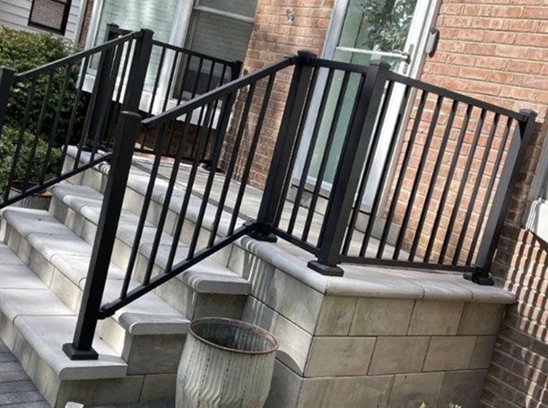 A black railing is on the steps of a brick house