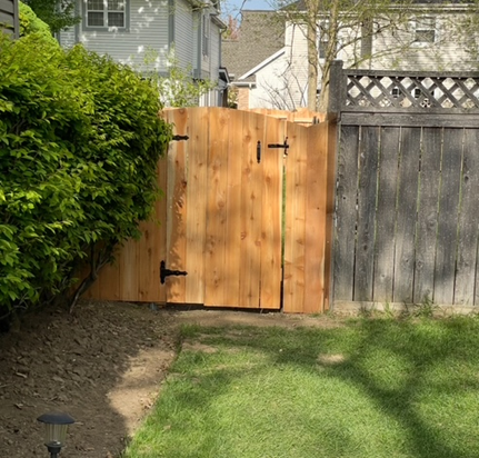 A wooden fence with a gate in the middle of a lush green yard.