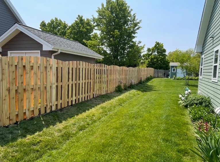 A wooden fence surrounds a lush green yard in front of a house.