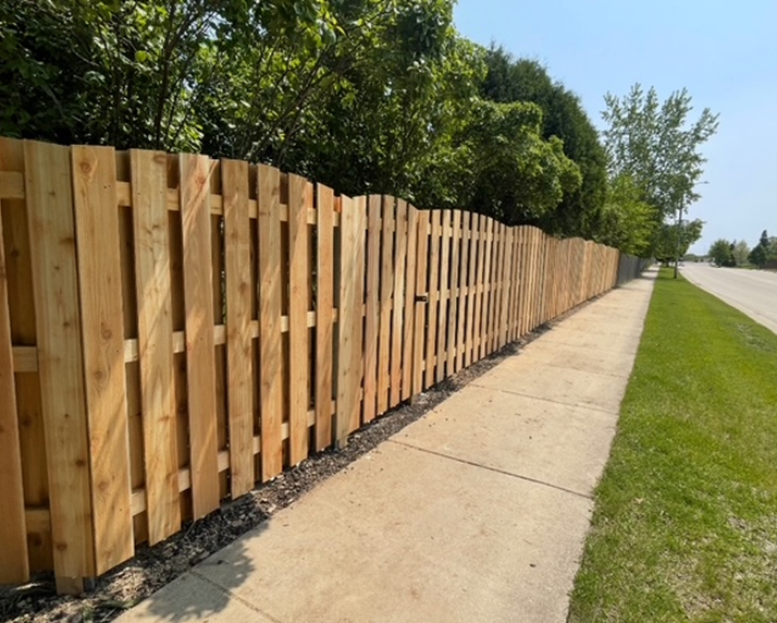 A wooden fence along a sidewalk with trees in the background