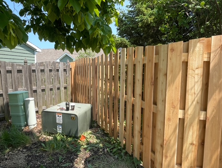A wooden fence surrounds a green box in a backyard.