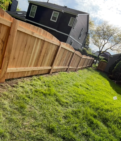 A wooden fence is sitting on top of a grassy hill in front of a house.