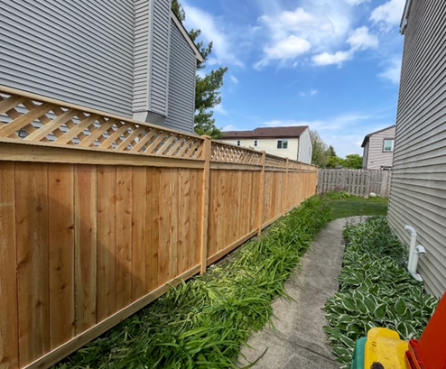 A wooden fence surrounds a concrete walkway between two houses.