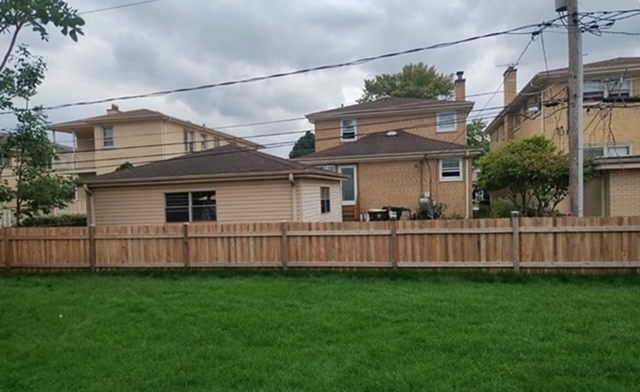 A wooden fence surrounds a lush green yard in front of a house.