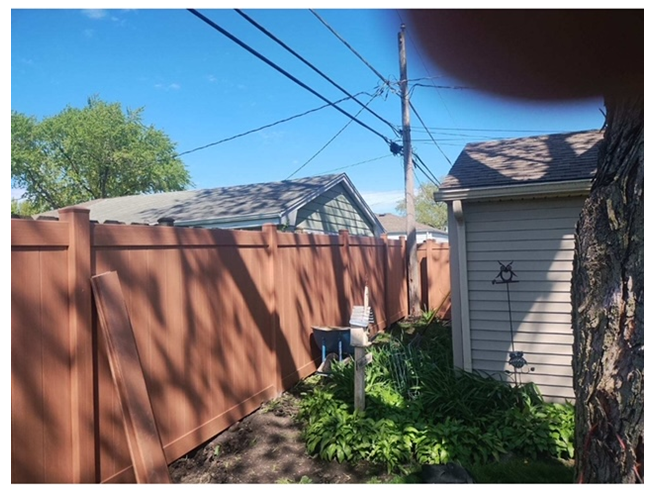 A wooden fence surrounds a house and a shed