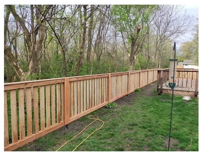 A wooden fence surrounds a lush green yard with trees in the background.