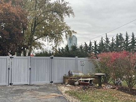 A white fence surrounds a yard with a picnic table and trees.