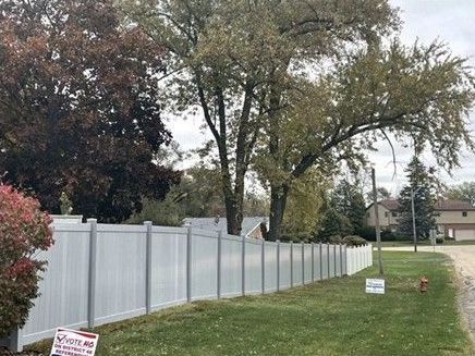 A white vinyl fence surrounds a lush green yard.