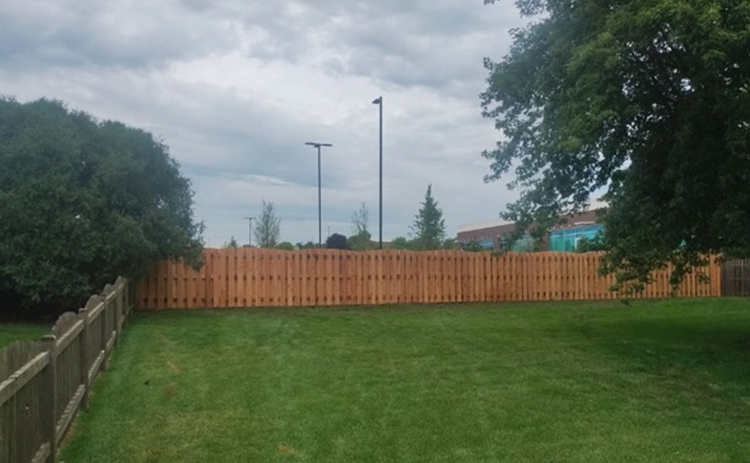 A wooden fence surrounds a lush green yard.