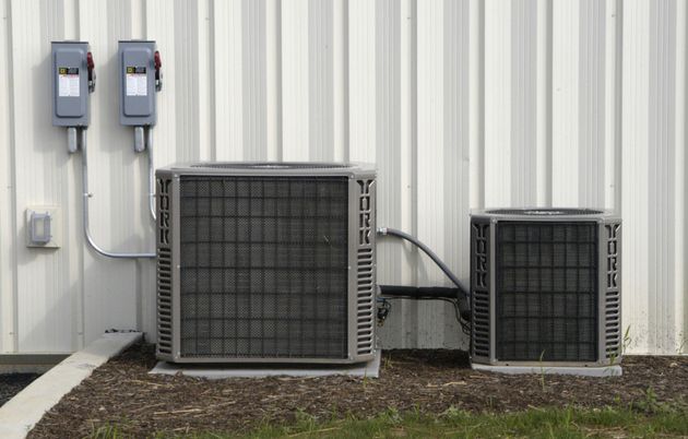 Two outdoor HVAC units beside a building wall with electrical boxes and conduit