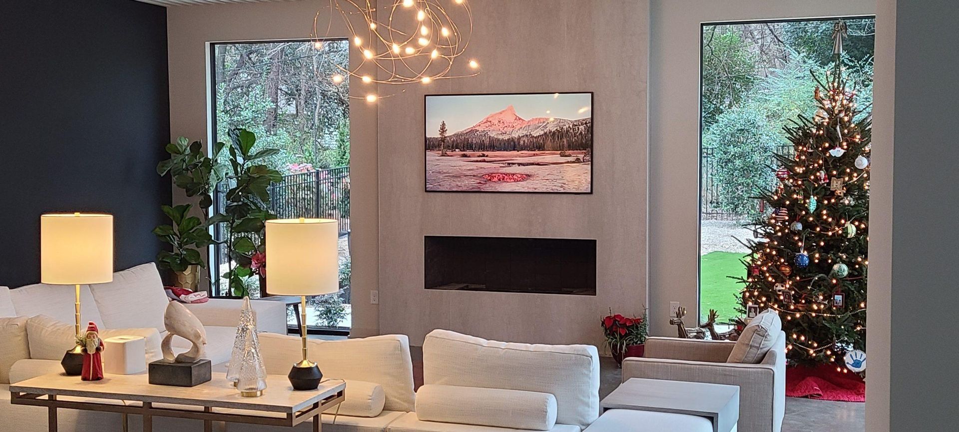Living room with a Christmas tree. White sofas, lamps, a painting, and a fireplace are present.