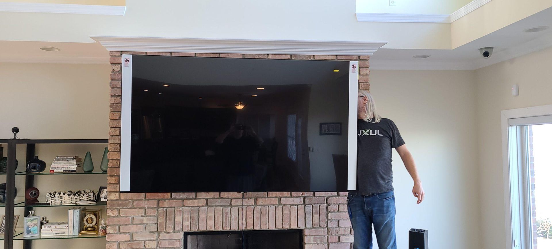 A person standing near a large television mounted above a fireplace, in a living room.