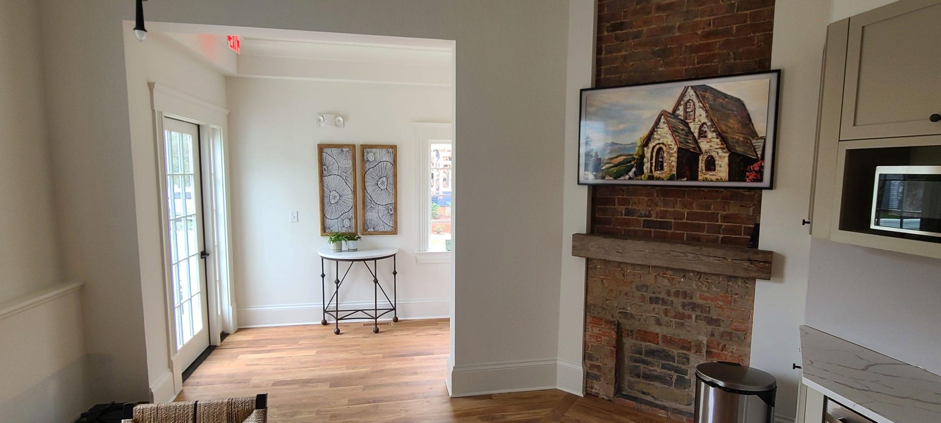 A room with a brick fireplace, a mounted TV, and cabinets, with a doorway leading to another room.